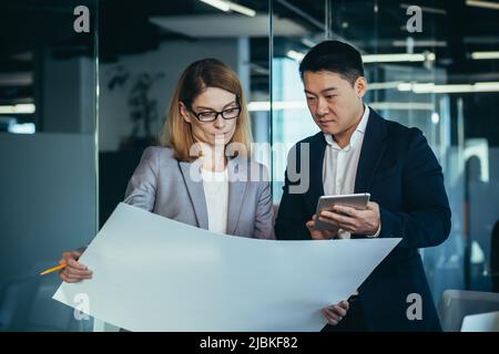 Group young creative engineers Developers discussing new project standing in modern office reading a blueprint. Team thoughtful architect designer. As Stock Photo