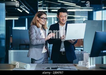 A team of multiracial business architects and designers discuss creating a project draft drawing by looking at laptop monitor screen a computer desk. Stock Photo
