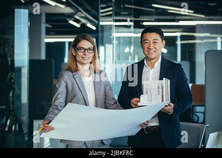 Team of two architects working on house plan project, asian man and woman looking successful at camera and smiling Stock Photo