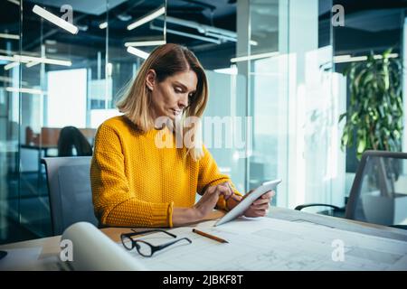Experienced female architect freelancer works in a modern office on drawings, uses a tablet Stock Photo