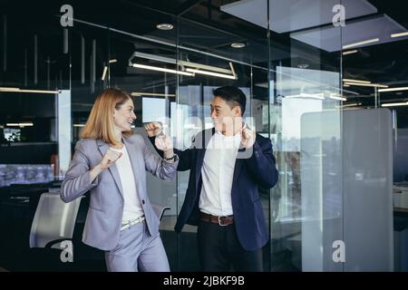 Two business people celebrating a successful deal, dancing in the office, Asian man and blonde woman Stock Photo