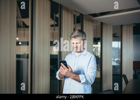 Successful man uses mobile app on phone for dating, experienced and gray-haired businessman in office Stock Photo