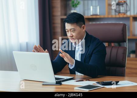 Asian businessman boss talking to colleagues on video call, looking at laptop screen, working in office, online meeting Stock Photo