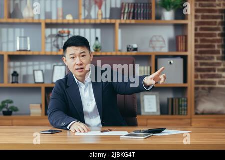 Asian angry businessman, boss fires employee looking at camera and pointing direction at door Stock Photo
