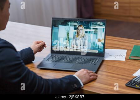Asian businessman looking at laptop screen, video call on webcam, boss working in office, talking to female colleague Stock Photo