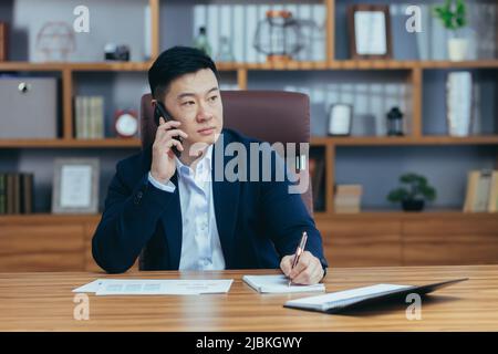 Successful Asian businessman working in the office, paperwork, talking on the phone Stock Photo