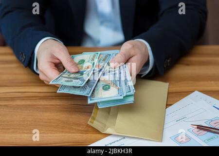 Close up photo hands of young businessman man holds and opens envelope with money, dollars, currency, holds in hands at table, shows, counts Stock Photo