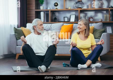 Senior couple man and woman together at home practicing yoga meditating sitting on the floor in lotus position Stock Photo