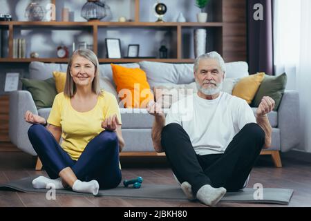 Senior couple man and woman together at home practicing yoga meditating sitting on the floor in lotus position Stock Photo