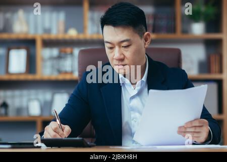 Close-up photo of businessman in office working on paper, serious and focused asian boss signing documents Stock Photo