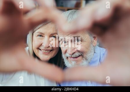 Joyful senior couple making heart shape with their hands while ...