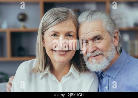 portrait of close up happy senior gray haired, married couple looking at camera while standing in room at home. Indoor. Husband and wife retirees smil Stock Photo