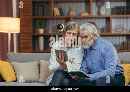 Happy senior couple husband and wife having fun together at dinner, reading a book and e-book, using a tablet reading application Stock Photo