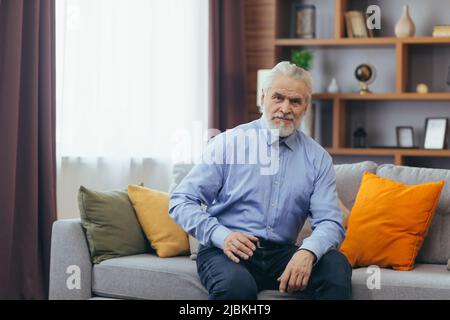 Serious for pensive grandfather man sitting on sofa at home Stock Photo