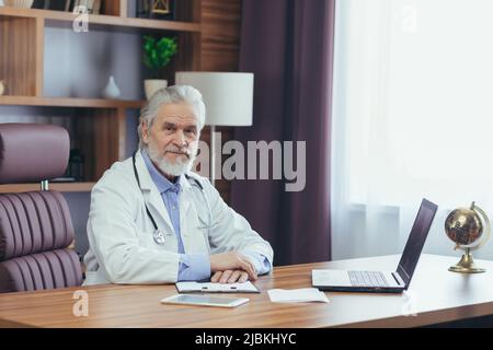 Portrait of a senior experienced doctor gray-haired man working in the office, looking at the camera Stock Photo