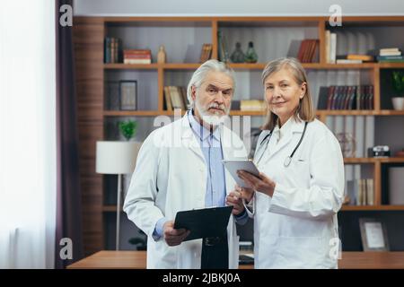 Gray-haired fellow doctors, male and female doctors work together in a classic clinic office, experienced doctors look into the camera Stock Photo
