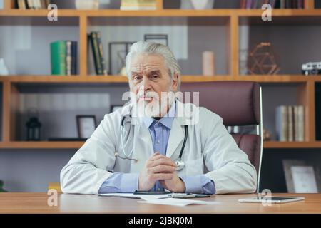Portrait of a senior experienced doctor gray-haired man working in the office, looking at the camera Stock Photo