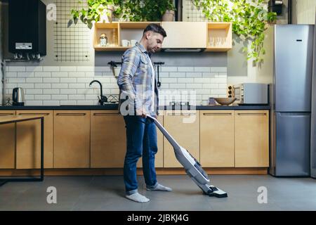 A young man cleans the apartment with a vacuum cleaner. Stock Photo