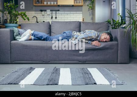 Very tired young man, student, freelancer lying on the couch at home, sleeping, resting. Stock Photo