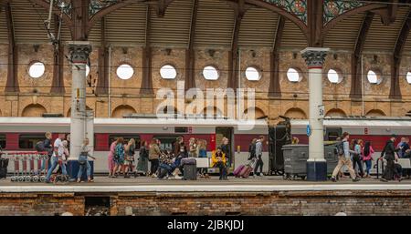 Passengers walk along a railway station platform after alighting from a train. Carriages are behind. Stock Photo