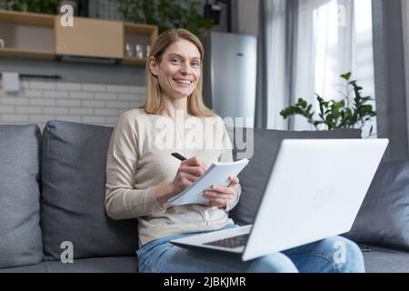 Portrait of woman at home, student recording lesson, using laptop for online training, sitting on sofa Stock Photo
