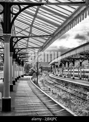 A train rests at a platform with a historic canopy. Crew members and ...