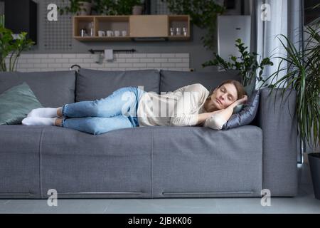 Tired middle aged blonde woman sleeping on sofa after work Stock Photo