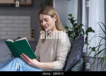 Beautiful woman relaxing at home after work, reading an interesting book sitting on the couch Stock Photo