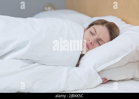 Close-up photo of a sleepless and upset woman lying in bed under a blanket, trying to fall asleep Stock Photo