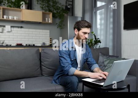 Focused and serious man at home working on laptop sitting on sofa Stock Photo
