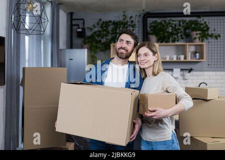 Happy couple man and woman live together, moved to a new rented apartment, holding cardboard boxes Stock Photo