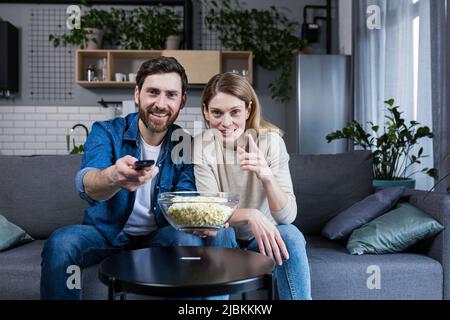 family happy couple man and woman eating popcorn and watching tv sitting on sofa at home Stock Photo