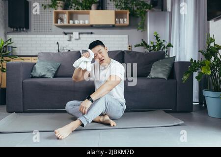 Happy man is resting after morning exercise, Asian is doing fitness at home on a sports mat Stock Photo