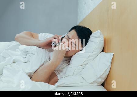 A sick man is at home, has a cold and flu, an Asian calls a doctor for help Stock Photo