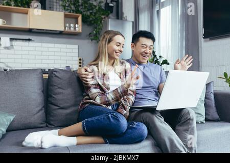 Happy young asian couple bonding laughing using laptop sit at table home Stock Photo