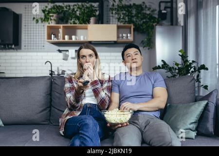 Couple man and woman at home watching TV together, bored switching channels, trying to find an interesting channel, family sitting on sofa at home Stock Photo