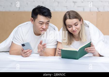 Photo close up of a happy family reading a book together lying on a bed under a blanket, man and woman happy couple together Stock Photo