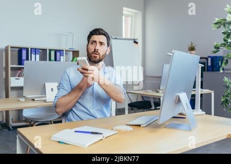 Businessman works during the day in a modern bright office, a man coldly holds a remote control from the air conditioner, raises the temperature Stock Photo