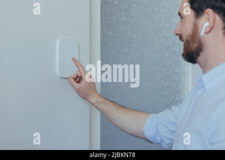Businessman enters finger password lock code on alarm panel, on white wall, rear view of man with beard Stock Photo