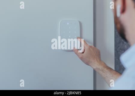 Businessman enters finger password lock code on alarm panel, on white wall, rear view of man with beard Stock Photo
