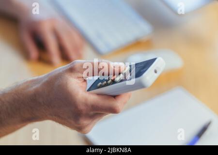 Close-up photo of a man's hand holding an air conditioner remote control, changing the temperature, businessman working in a bright office Stock Photo
