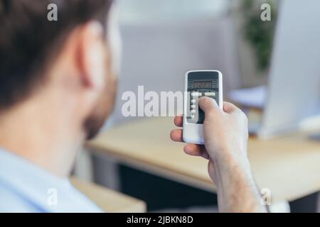 Close-up photo of a man's hand holding an air conditioner remote control, changing the temperature, businessman working in a bright office Stock Photo