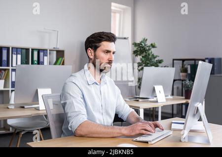 Concentrated and pensive businessman working in the office at the computer, paperwork broker, man looking at the monitor Stock Photo