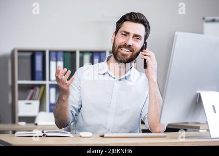 Successful male programmer working in the office at the computer talking to colleagues on the phone smiling. Stock Photo