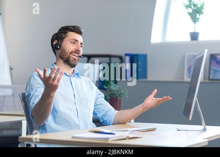 A happy surprised call center employee works in the office with a headset for a video call Stock Photo