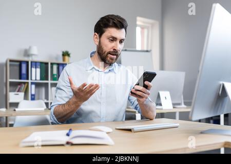 surprised and shocked businessman in the office, man looks at the phone screen, reads the news online Stock Photo