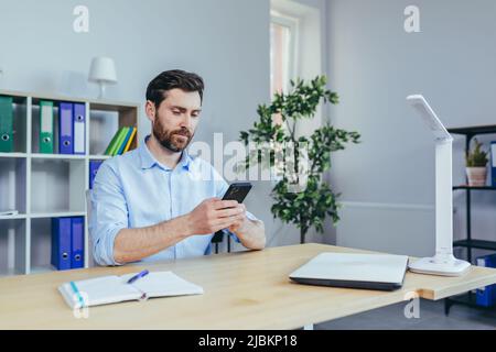 Serious bearded businessman carefully reads the news from the phone, working in the office Stock Photo