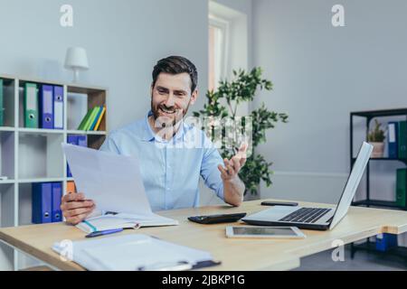 Happy businessman working with papers, working on laptop, man at work in a bright office Stock Photo