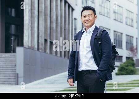 Successful asian business tourist looking at camera and smiling, man in business suit and backpack Stock Photo