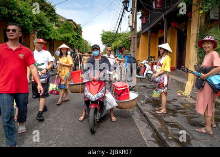 Hoi An Ancient Town, Quang Nam Province, Vietnam - April 30, 2022: A man rides a motorbike with a pair of rattan bamboo frame on his shoulders in Hoi Stock Photo